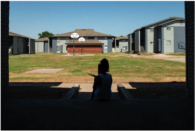 A child sits on the steps of an east Tulsa apartment complex on June 15 reading a flyer that has information about rental assistance. (Whitney Bryen/Oklahoma Watch)