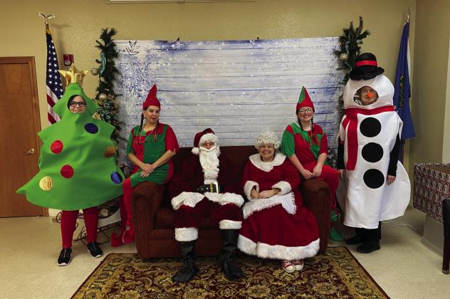 Courtesy photos Top left: Mrs. Claus reads to the children. Top right: Santa, Mrs. Claus, their helpers and Christmas cheer. Bottom left: Santa poses with two children. Bottom right: Santa's helpers and local children.