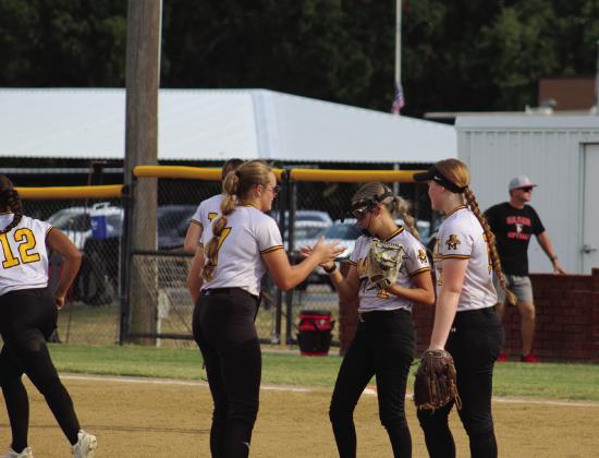 Pictured left: Kinsley Troxtell hits the ball to the outfield. Pictured right: The Lady Wildcats hype each other up for the game. Courtesy photos